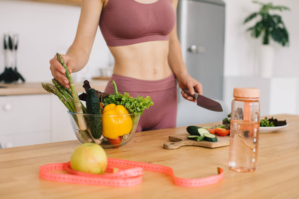 Sporty woman preparing fresh vegetable salad in the kitchen, healthy eating concept - Photo, Image
