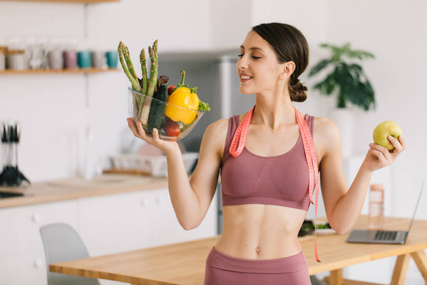 Portrait de femme sportive heureuse tenant pomme et assiette de légumes frais, concept de saine alimentation - Photo, image