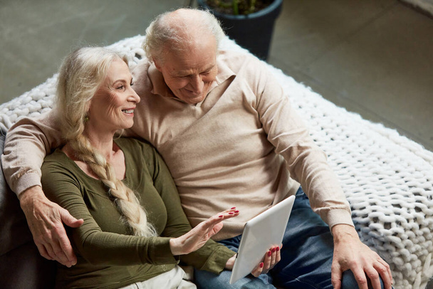 Top view image of lovely happy old couple, middle-aged man and woman sitting on sofa at home and watching on tablet. Online shopping. Concept of family, relationship, retirement, lifestyle, happiness - Valokuva, kuva