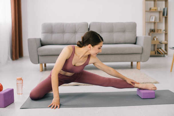 Mujer joven atractiva y saludable haciendo ejercicios mientras descansa en casa
 - Foto, Imagen