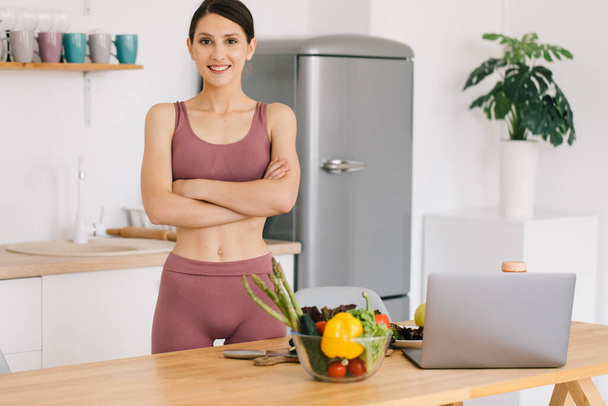 Портрет счастливой спортивной женщины-блоггера за столом со свежими овощами, концепция здорового питания - Фото, изображение