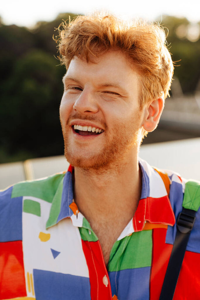 Portrait of young handsome smiling happy winking man in colorful shirt looking at camera , while standing in the sun - Valokuva, kuva