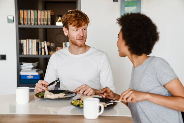 Joven hermosa pareja interracial mirándose y desayunando juntos en casa - Foto, imagen