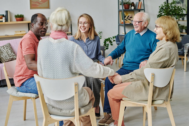 Groep gelukkige ouderen zit op stoelen en werkt met psycholoog in therapie in verpleeghuis - Foto, afbeelding