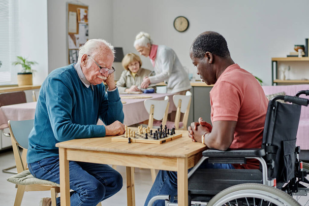 Uomo anziano che gioca a scacchi insieme al suo amico con disabilità, passano il tempo in casa di cura - Foto, immagini