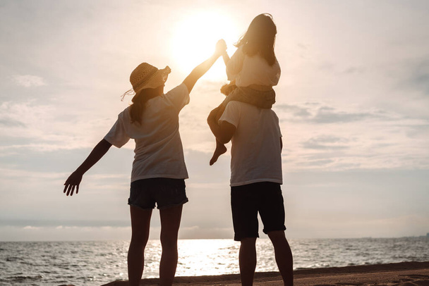 Happy asian family enjoy the sea beach at consisting father, mother and daughter having fun playing beach in summer vacation on the ocean beach. Happy family with vacations time lifestyle concept. - 写真・画像