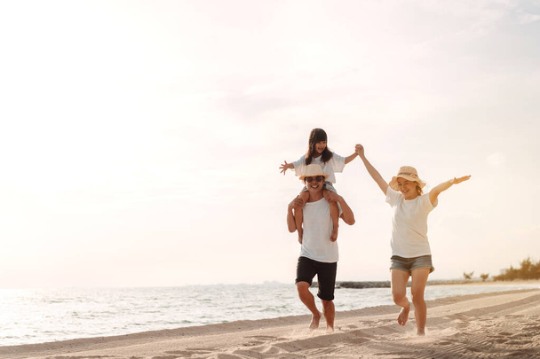Happy asian family enjoy the sea beach at consisting father, mother and daughter having fun playing beach in summer vacation on the ocean beach. Happy family with vacations time lifestyle concept. - Photo, image