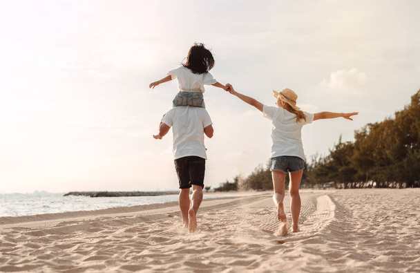 Happy asian family enjoy the sea beach at consisting father, mother and daughter having fun playing beach in summer vacation on the ocean beach. Happy family with vacations time lifestyle concept. - 写真・画像