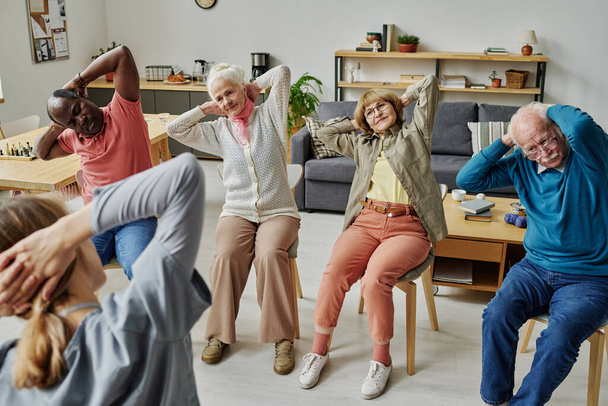 Group of senior people exercising on chairs in nursing home together with instructor - Foto, Bild