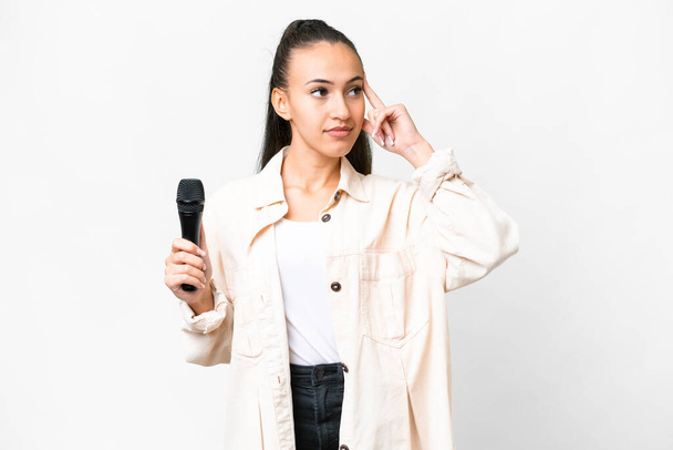 Nuori laulaja nainen poimien mikrofonin yli eristetty valkoinen tausta epäilee ja ajattelee - Valokuva, kuva
