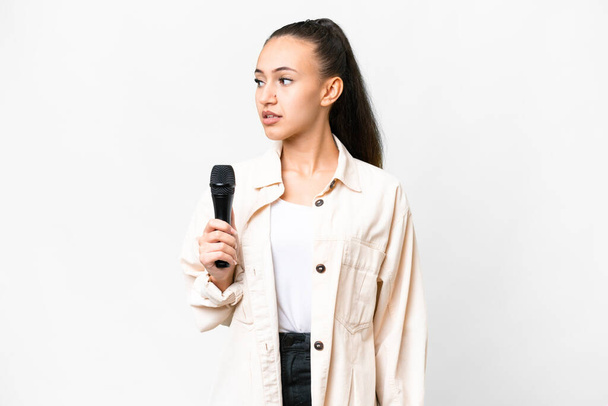Young singer woman picking up a microphone over isolated white background looking to the side - Photo, image