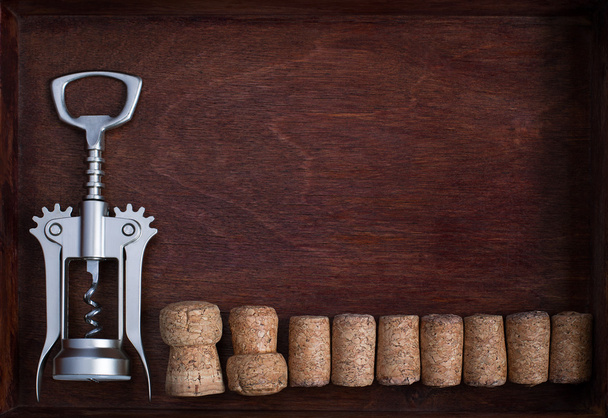 Corkscrew e uma fileira de rolhas de vinho em caixa escura
 - Foto, Imagem