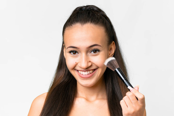 Young Arabian woman over isolated white background holding makeup brush and whit happy expression - Фото, изображение