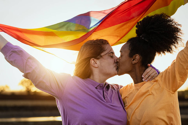 レズビアンカップルキスしながら保持虹のフラグ中にゲイ誇りお祝い屋外- Lgbtと愛平等の概念 - 写真・画像