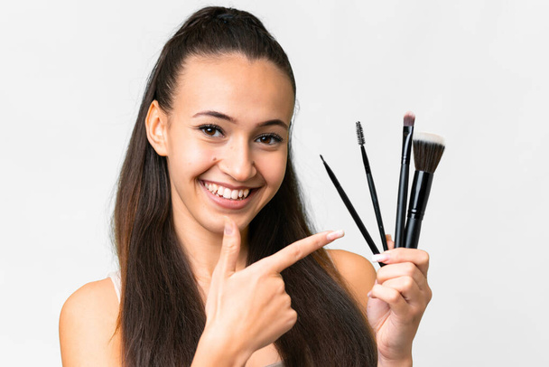 Young Arabian woman over isolated white background holding makeup brush and pointing it - Φωτογραφία, εικόνα