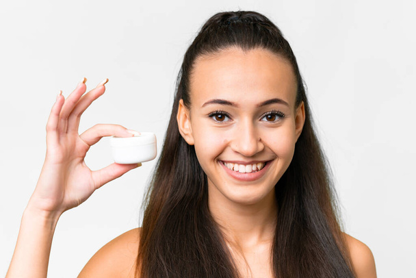 Jonge Arabische vrouw over geïsoleerde witte achtergrond met moisturizer - Foto, afbeelding