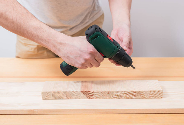 A man works with an electric screwdriver on a wooden table - Foto, Imagem