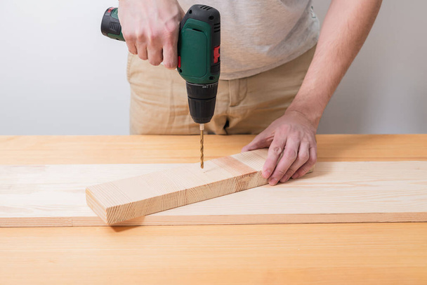 Un hombre trabaja con un destornillador eléctrico en una mesa de madera - Foto, imagen