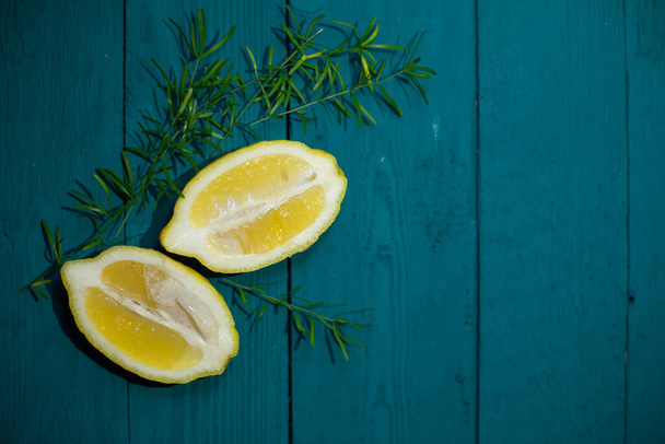 Two mats of juicy, fresh lemon with a sprig of greenery on a blue background with a wooden texture - Zdjęcie, obraz