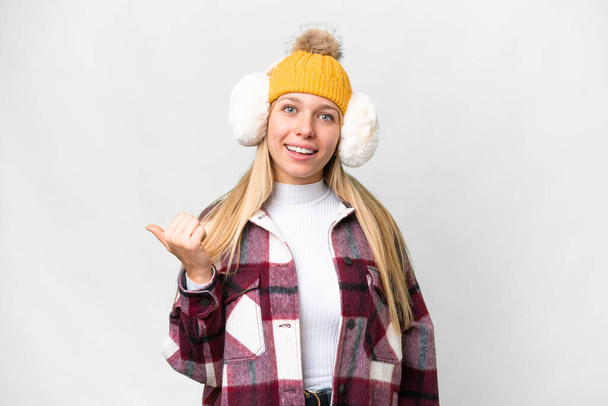 Young pretty blonde woman wearing winter muffs over isolated white background pointing to the side to present a product - Foto, Imagen