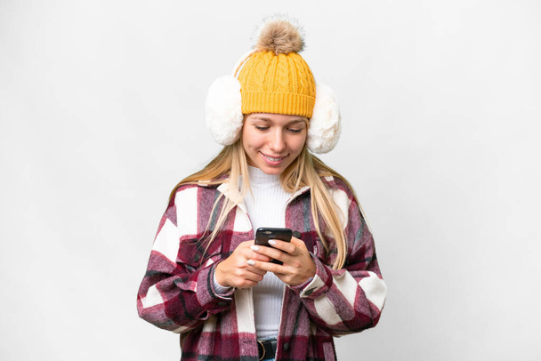 Молода красива блондинка в зимових муфтах над ізольованим білим тлом надсилає повідомлення з мобільним
 - Фото, зображення