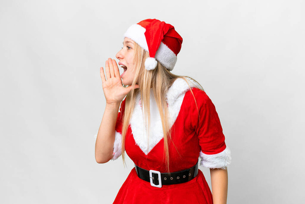Jeune femme blonde avec chapeau de Noël sur fond blanc isolé criant avec la bouche grande ouverte sur le côté - Photo, image