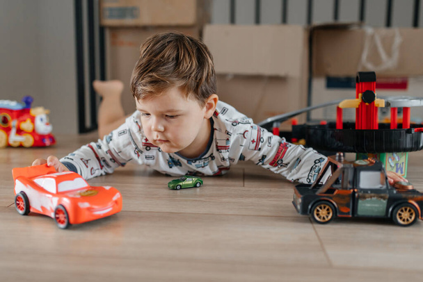 Happy little boy sitting on white carpet at home and playing with car toy. High quality photo - Fotoğraf, Görsel