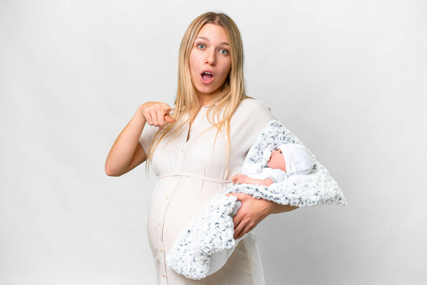 Young pretty pregnant woman with her newborn baby over isolated white background surprised and pointing front - Photo, Image