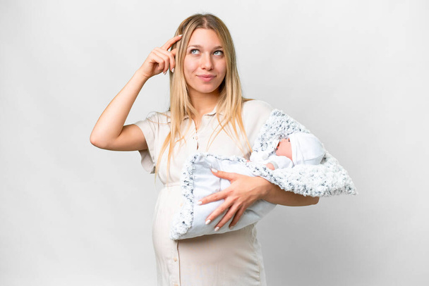 Young pretty pregnant woman with her newborn baby over isolated white background having doubts and with confuse face expression - Foto, Bild