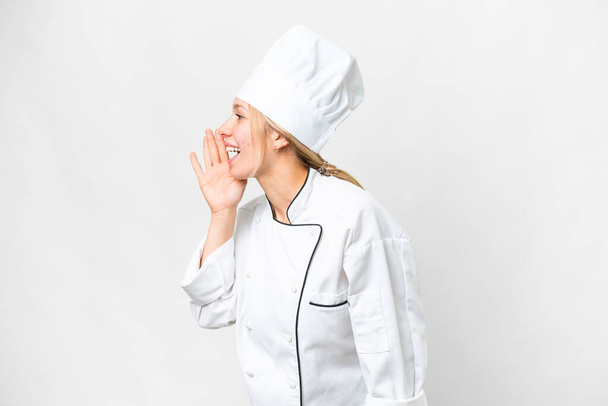 Young chef woman over isolated white background shouting with mouth wide open to the lateral - Foto, imagen