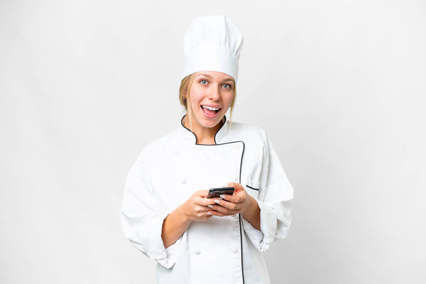 Giovane chef donna su sfondo bianco isolato sorpreso e l'invio di un messaggio - Foto, immagini