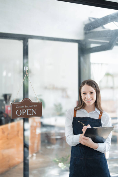 Kisvállalkozást indít és nyit, egy fiatal ázsiai nő mosolygós arcot mutat egy kötényben, amint egy kávézó pult előtt áll. Business Owner, Étterem, Barista, Kávézó, Online KKV. - Fotó, kép