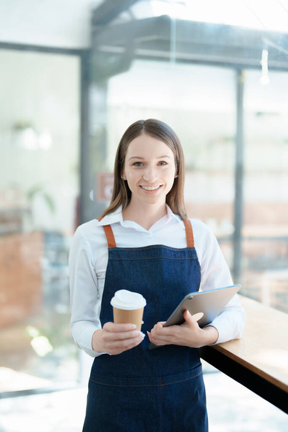 Starting and opening a small business, a young Asian woman showing a smiling face in an apron standing in front of a coffee shop bar counter. Business Owner, Restaurant, Barista, Cafe, Online SME. - Fotografie, Obrázek