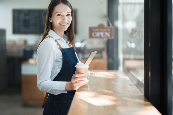 Küçük bir işletme kuran ve açan genç bir Asyalı kadın, kafeterya tezgahının önünde duran önlüklü gülen bir yüz gösteriyor. İş sahibi, Restoran, Barista, Cafe, Çevrimiçi KOBİ. - Fotoğraf, Görsel