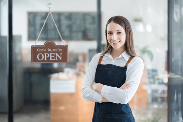コーヒーショップのカウンターの前に立つエプロンに笑顔を見せる若いアジア人女性が小さなビジネスを始め、開業します。ビジネスオーナー,レストラン,バリスタ,カフェ,オンライン中小企業. - 写真・画像