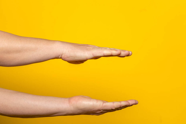 Сильные руки человека параллельно предлагают что-то воображаемое внутри, рекламное понятие с копировальным пространством. Изолированный на желтом фоне - Фото, изображение