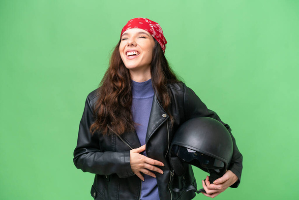 Молода біла жінка з мотоциклетним шоломом над ізольованим тлом багато посміхається
 - Фото, зображення