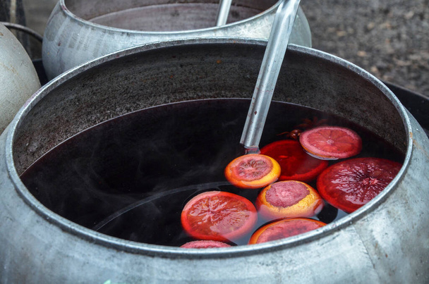Hot mulled wine at the fair brewed in a cauldron with with red wine and citrus - Fotografie, Obrázek