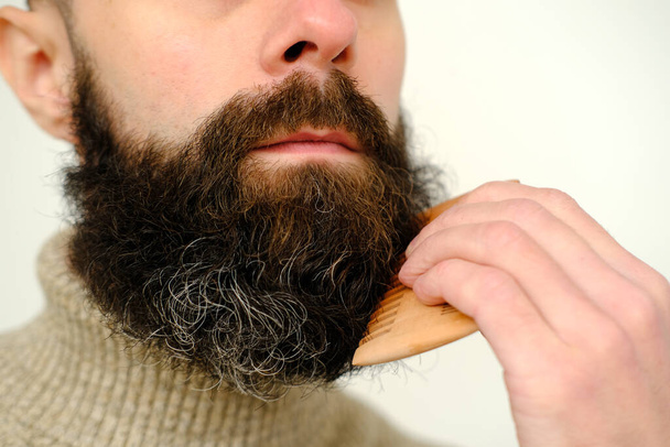 close-up of male face, young bearded and mustachioed man, guy with 25 - 30 years combs his thick beard, concept of mustache and beard stubble care products, hairline hygiene on lower part of face - Photo, Image