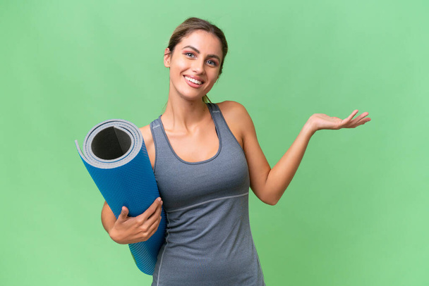 Pretty Young Uruguayan sport woman going to yoga classes while holding a mat over isolated background extending hands to the side for inviting to come - Foto, Imagem