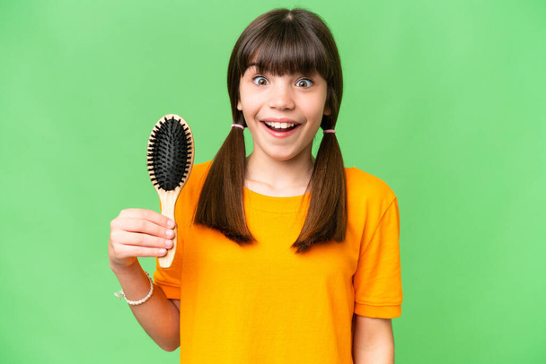 Μικρό καυκάσιο κορίτσι με χτένα μαλλιών πάνω από απομονωμένο φόντο με έκπληξη και σοκαρισμένη έκφραση προσώπου - Φωτογραφία, εικόνα