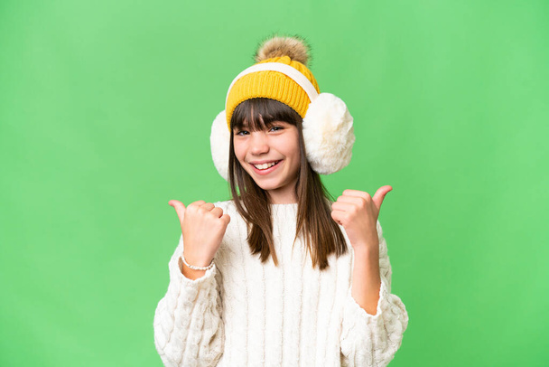 Little caucasian girl wearing winter muffs over isolated background with thumbs up gesture and smiling - Foto, Imagen