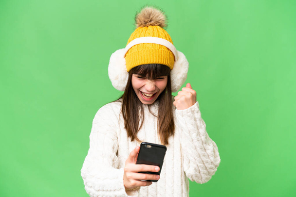 Pequeña chica caucásica con manguitos de invierno sobre fondo aislado sorprendido y enviando un mensaje - Foto, Imagen