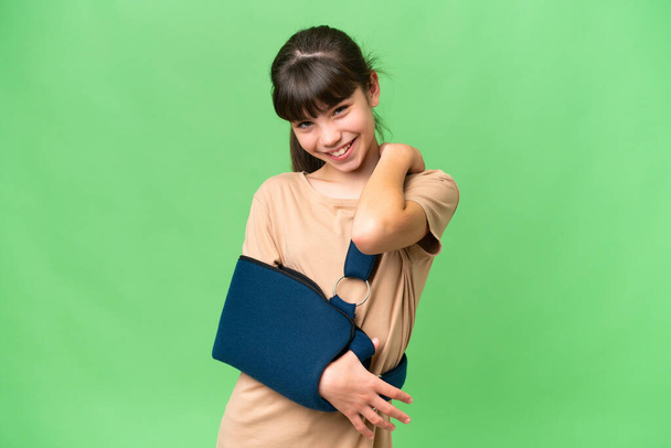 Klein blank meisje met gebroken arm en het dragen van een sling over geïsoleerde achtergrond lachen - Foto, afbeelding