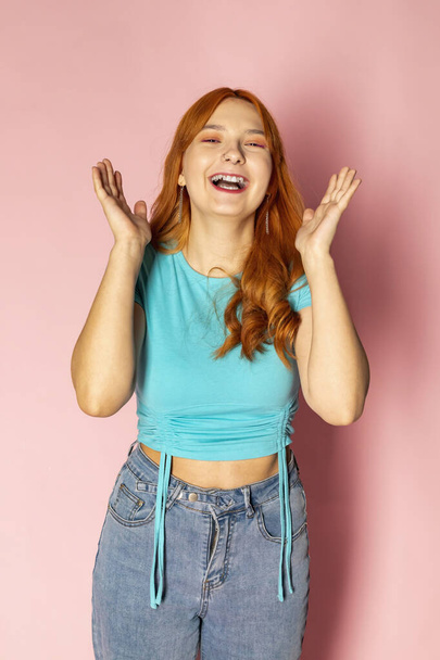 A happy red-haired young girl is laughing against an isolated pink background. - Valokuva, kuva