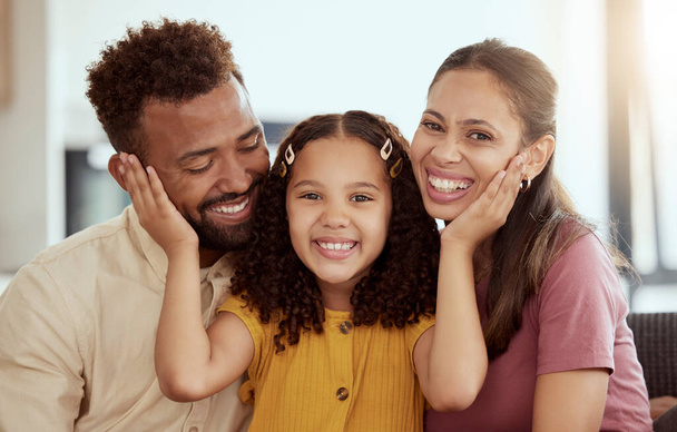 Mixed race parents enjoying weekend with daughter in home living room. Smiling hispanic girl hugging and bonding with mother and father in lounge. Happy affectionate couple sitting together with chil. - 写真・画像