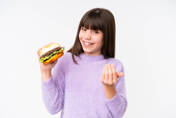 Kleine kaukasische Mädchen mit einem Burger über isoliertem Hintergrund einladend, mit der Hand zu kommen. Glücklich, dass du gekommen bist - Foto, Bild