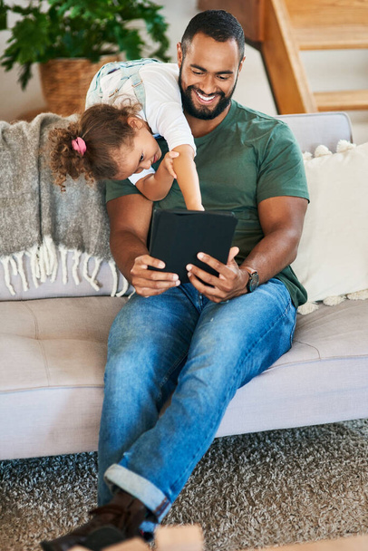 Ich möchte dieses Spiel jetzt spielen. Ein Vater und seine kleine Tochter nutzen zu Hause gemeinsam ein digitales Tablet - Foto, Bild