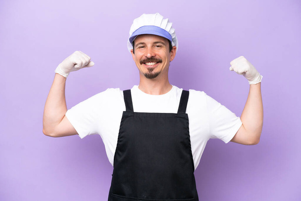 Fishmonger man wearing an apron isolated on purple background doing strong gesture - Foto, immagini