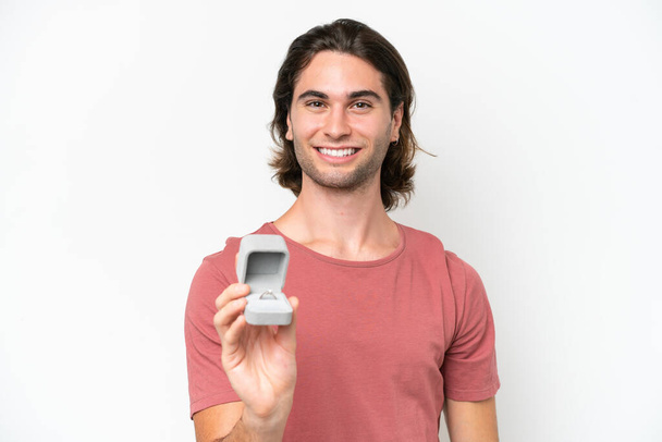 Mladý pohledný muž drží zásnubní prsten izolované na bílém pozadí se šťastným výrazem - Fotografie, Obrázek